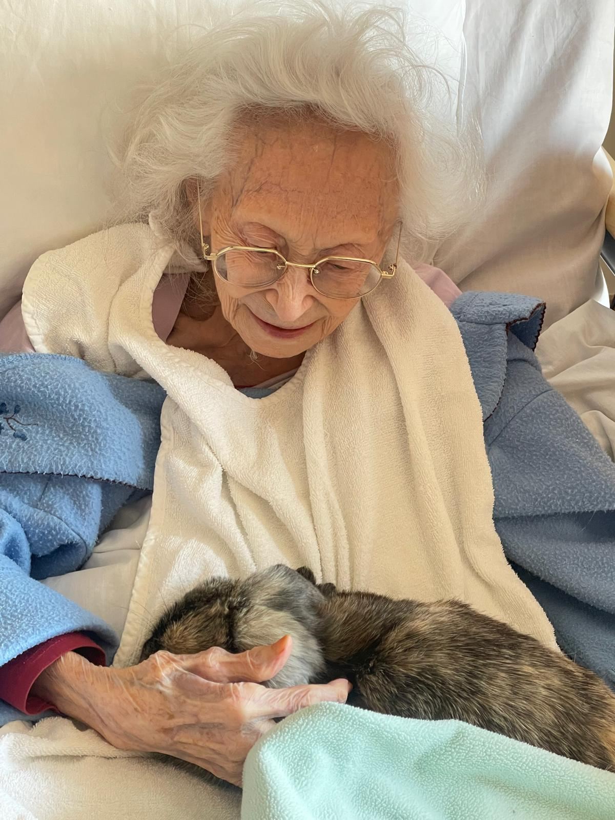 Une dame âgée tient tendrement un petit animal blotti contre elle dans une couverture