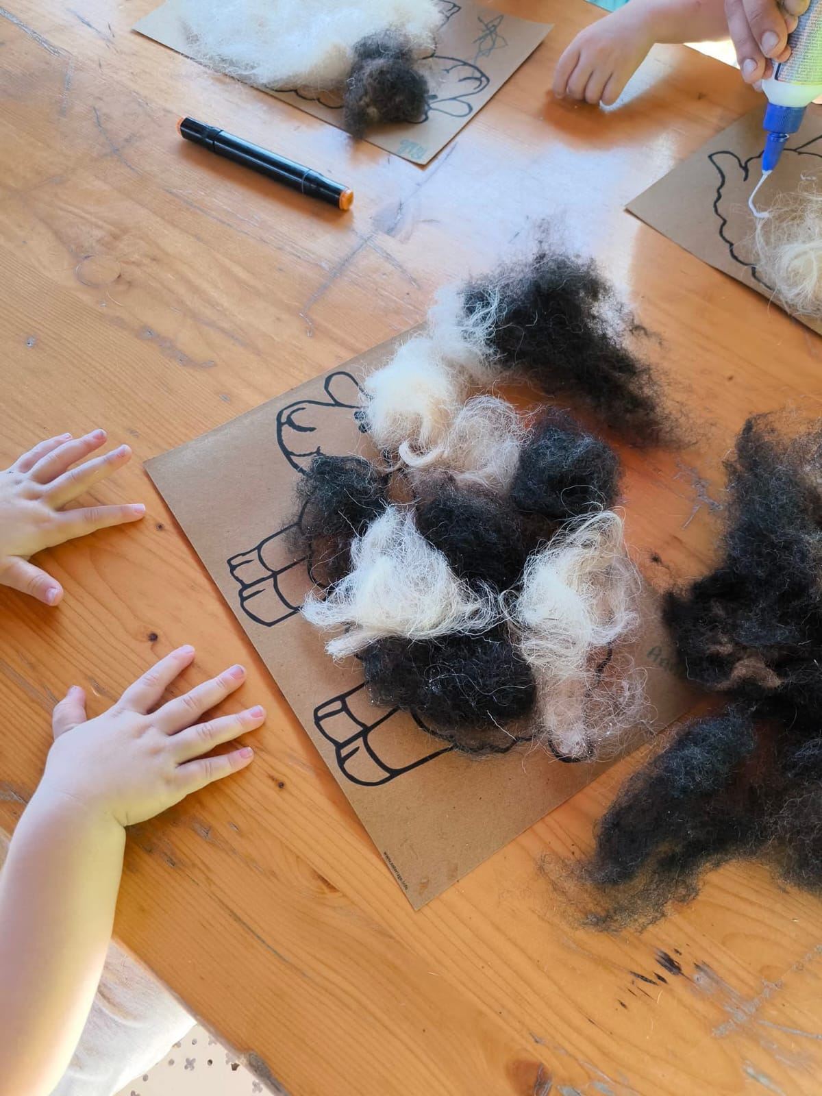 Atelier laine : des enfants collent de la laine sur des dessins de moutons en carton
